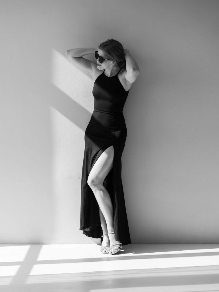 kobieta pod ścianą, w czarnej sukni, kobieca sesja zdjęciowa w studiu