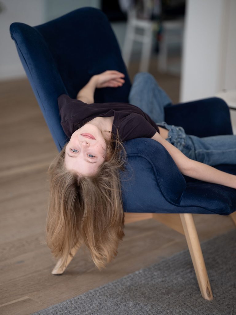 portret dziewczynki, blond włosy, wisi na fotelu do dołu głową